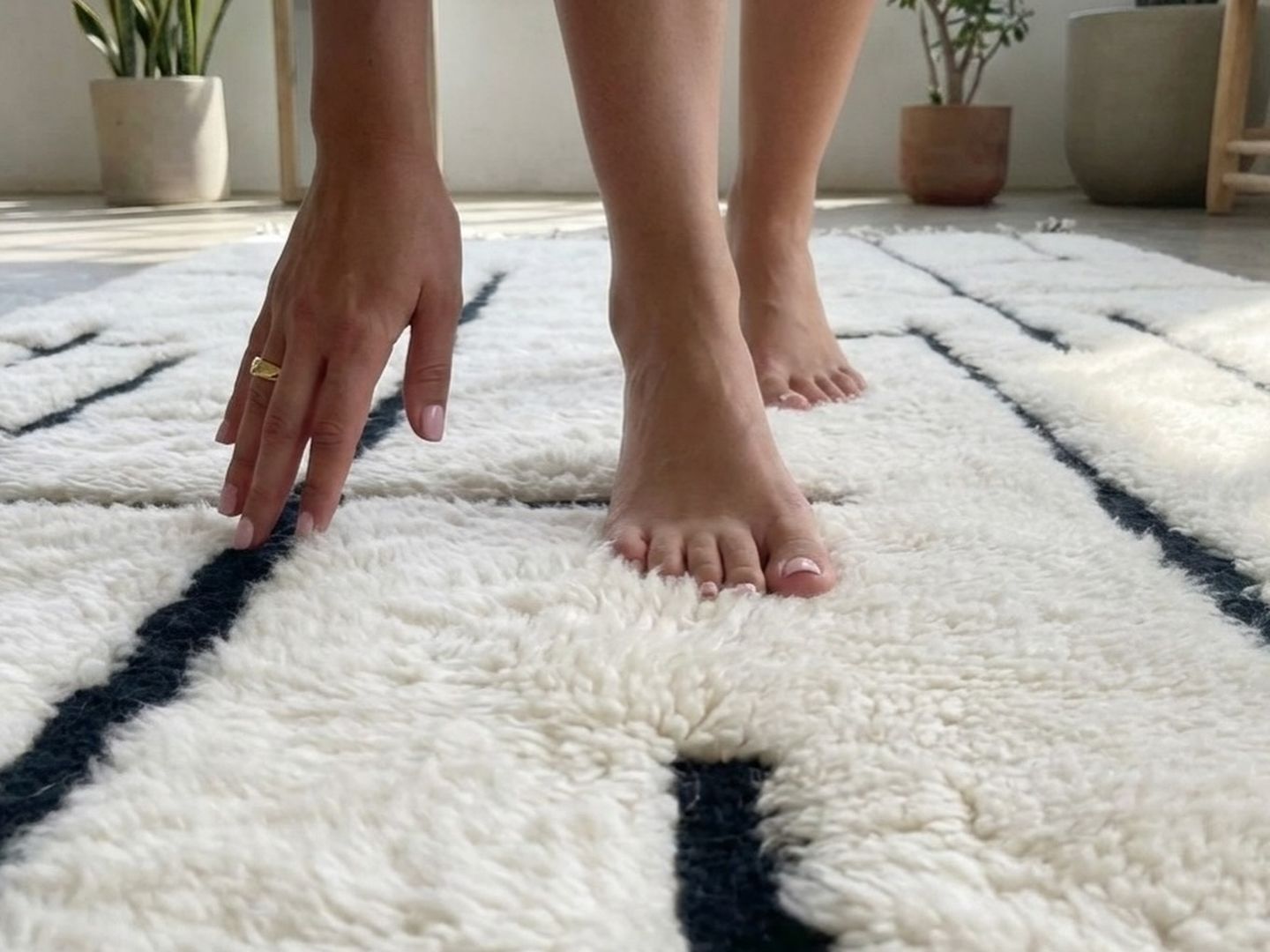 Pieds nus et main posée sur un tapis écru à motif labyrinthe noir